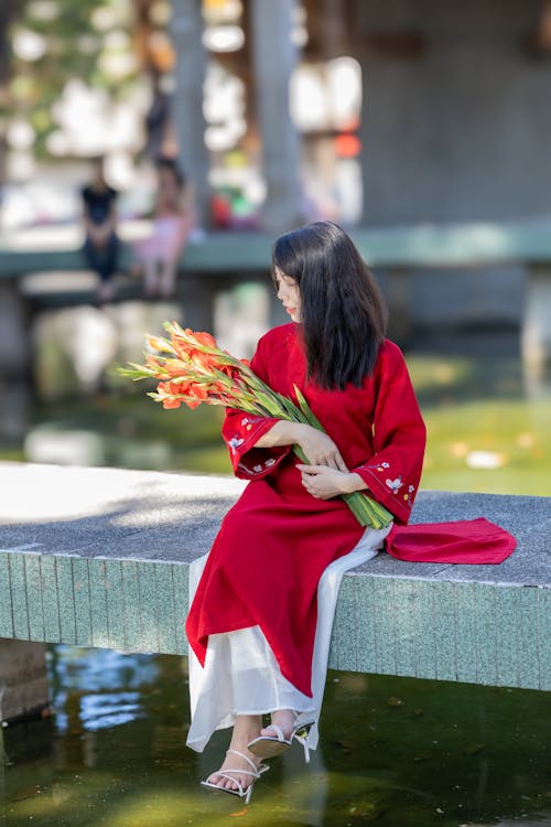 Model in a Red Ao Dai Tunic with Flower Embroidered Cuffs Holding an Armful of Flowers