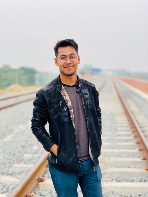 Free A man smiling on a railway track wearing a leather jacket, jeans, and eyeglasses. Stock Photo