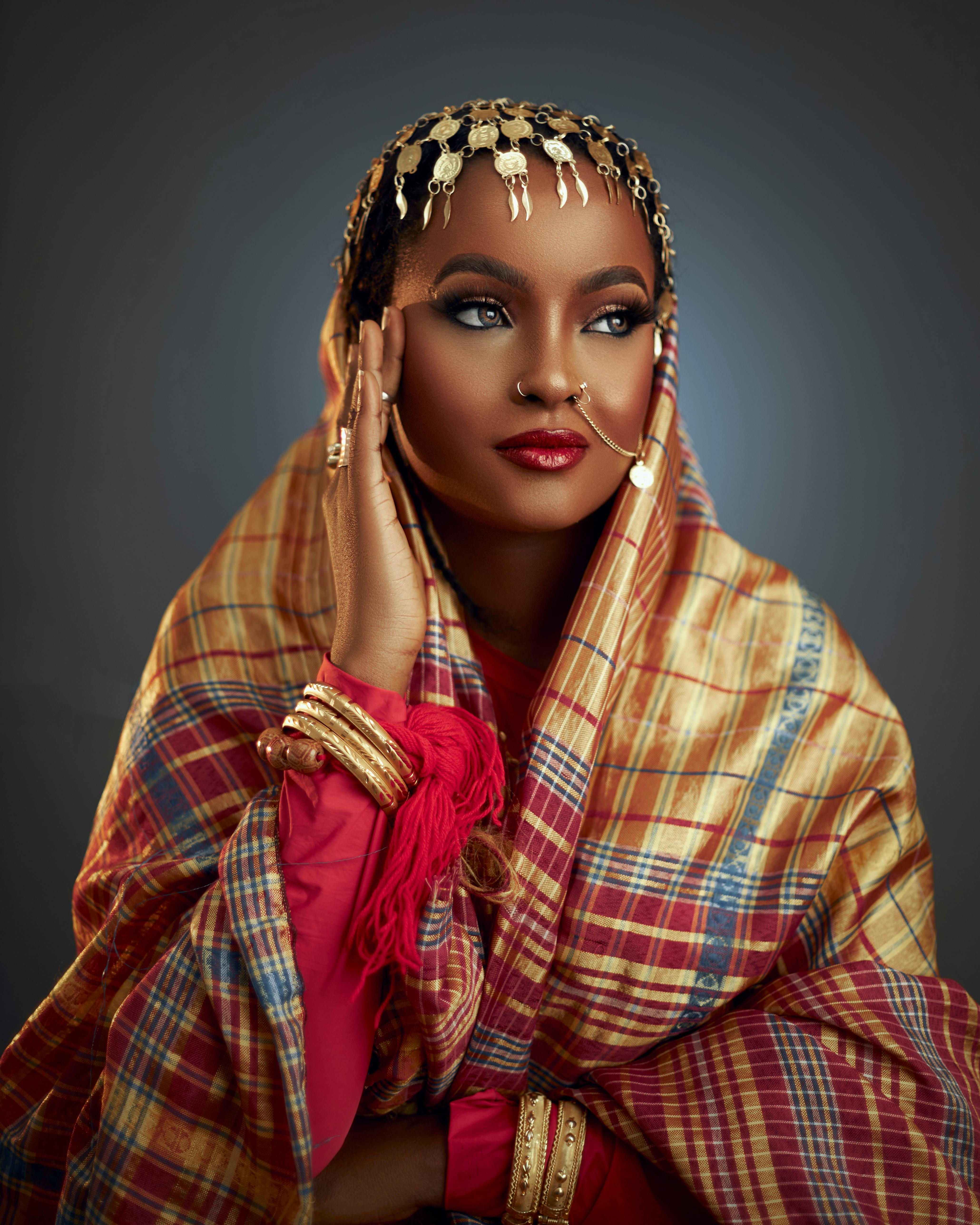 Portrait of a woman in traditional attire with gold jewelry on a gray background.