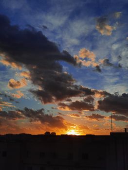 Breathtaking sunset with dramatic clouds over urban skyline, featuring vivid orange and blue hues.