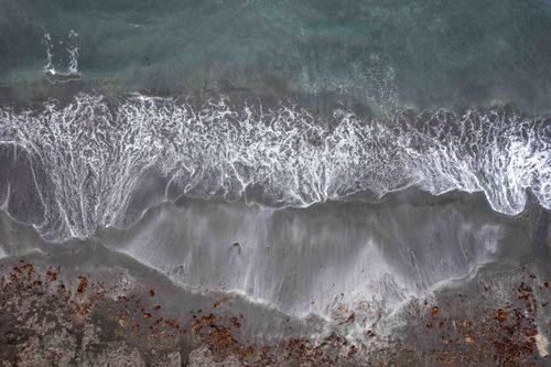 Free Captivating drone shot of ocean waves crashing on Húsavík black sand beach, Iceland. Stock Photo