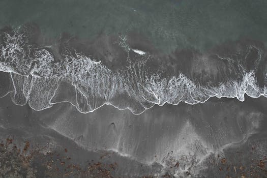 Stunning aerial shot of waves crashing on the black sand beach of Húsavík, Iceland.