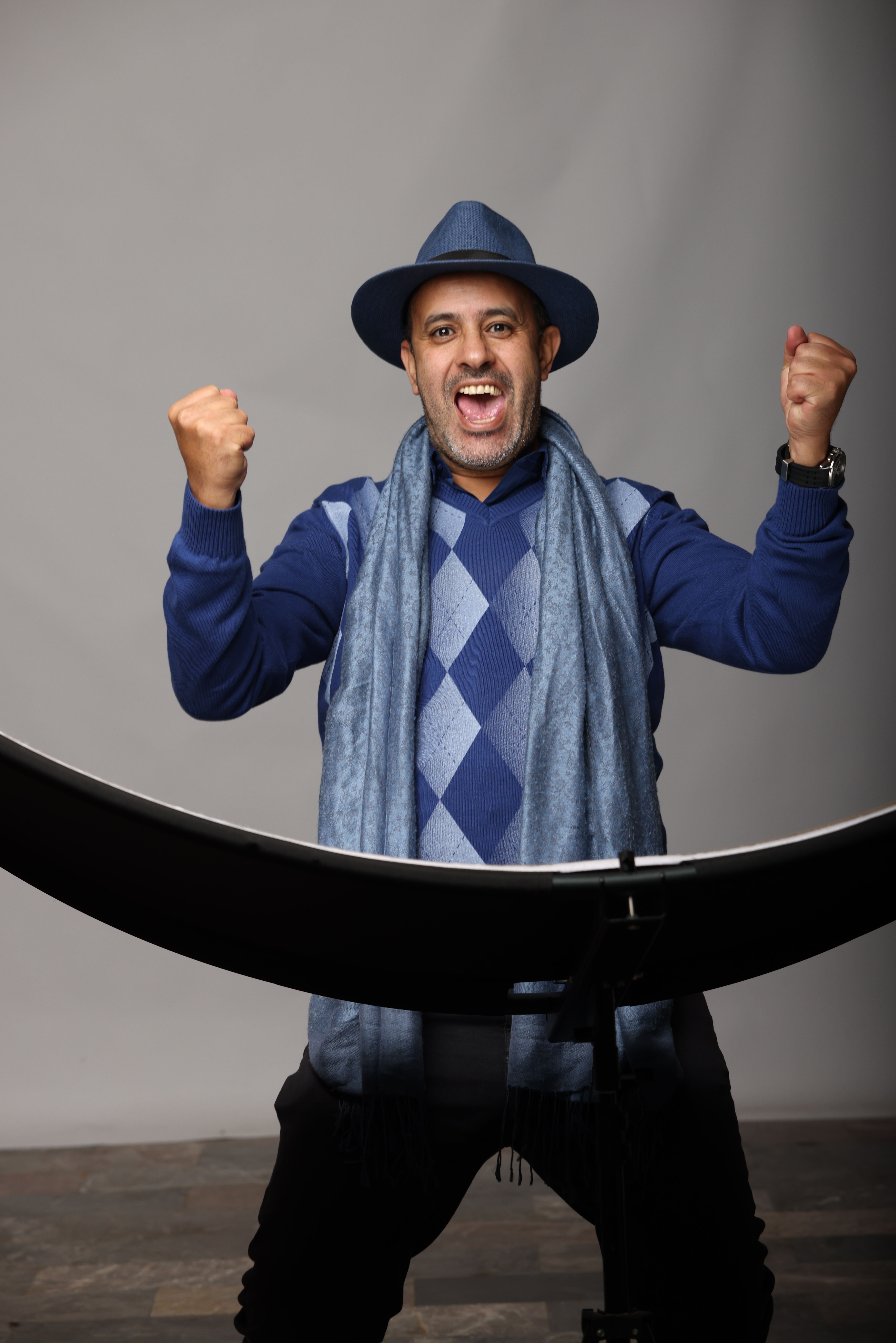 A joyful man in a stylish hat and scarf posing indoors, exuding warmth and excitement.