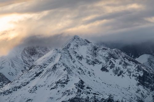 Free A breathtaking view of a snow-covered mountain peak under a dawn sky with fog and clouds. Stock Photo