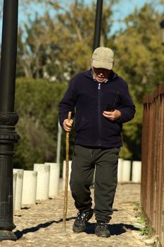Senior man enjoys a sunny outdoor stroll using a cane and smartphone.