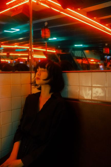 Young woman with closed eyes sitting under vibrant neon lights, creating a moody ambiance.