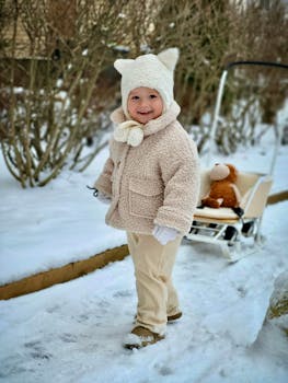 Adorable child in warm clothing pulling a toy sled on a snowy winter day, exuding joy and playfulness.