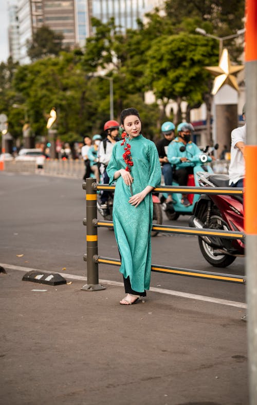 Woman in Turquoise Dress Posing on a Sidewalk with Red Flowers