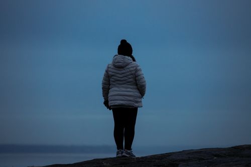 Free Silhouetted woman in a winter jacket standing outdoors, facing the horizon. Stock Photo