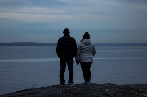 Free Couple facing a calm lake at twilight holding hands, evoking a serene and intimate moment. Stock Photo