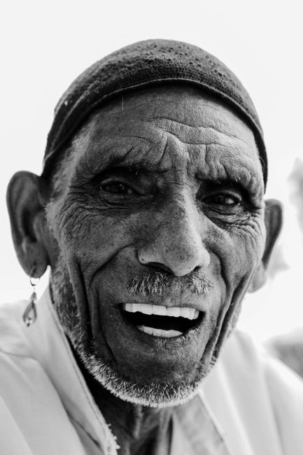 Close-up portrait of a senior man smiling warmly in a monochrome setting.
