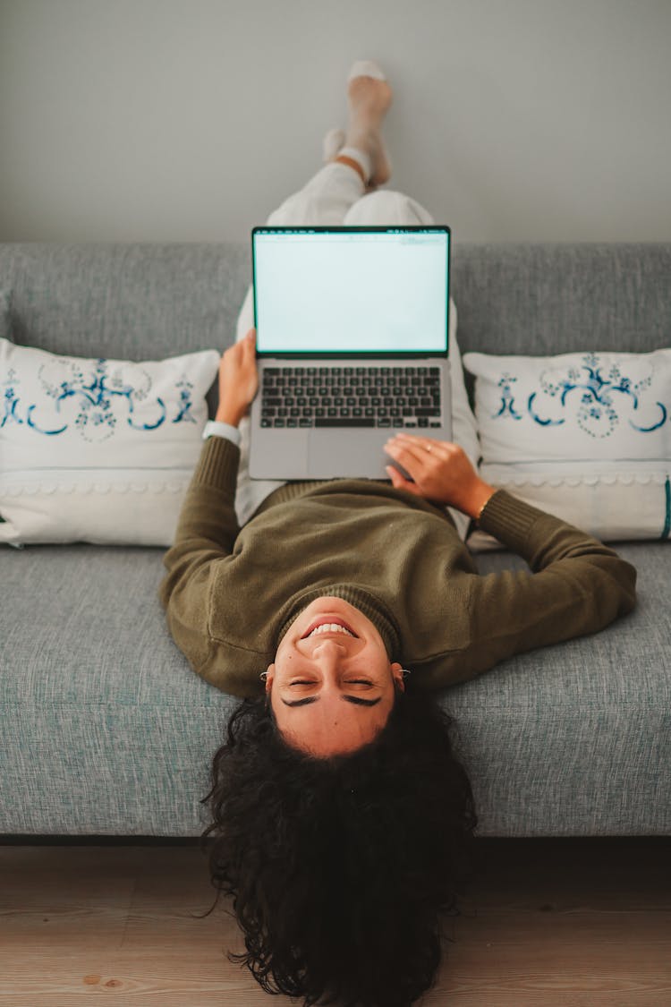 Young Woman Lying Upside Down On The Sofa With A Laptop