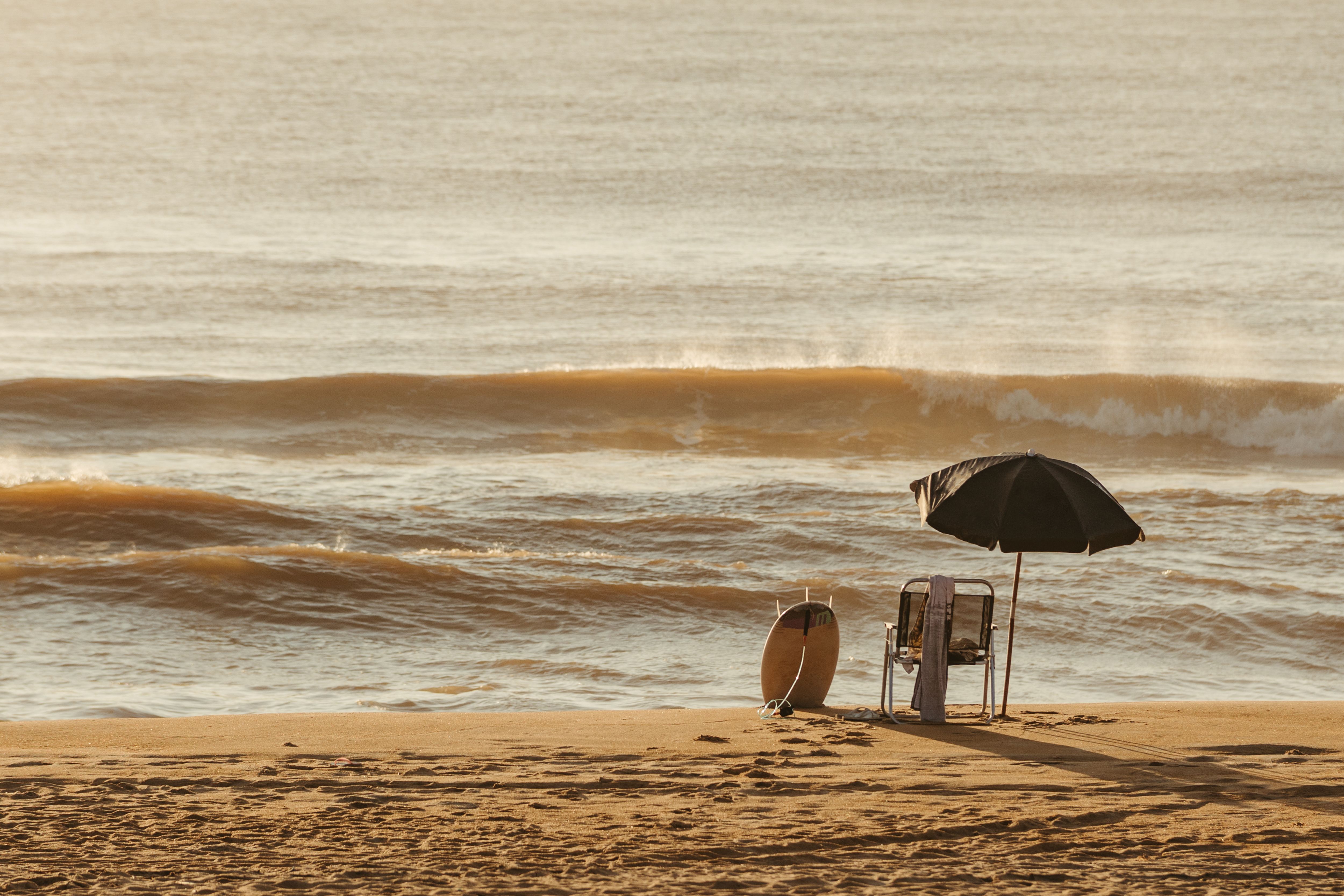 Beach chair, umbrella, and board beside ocean waves