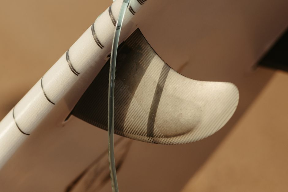 Detailed close-up of a surfboard fin captured in natural summer sunlight, perfect for beach themes.