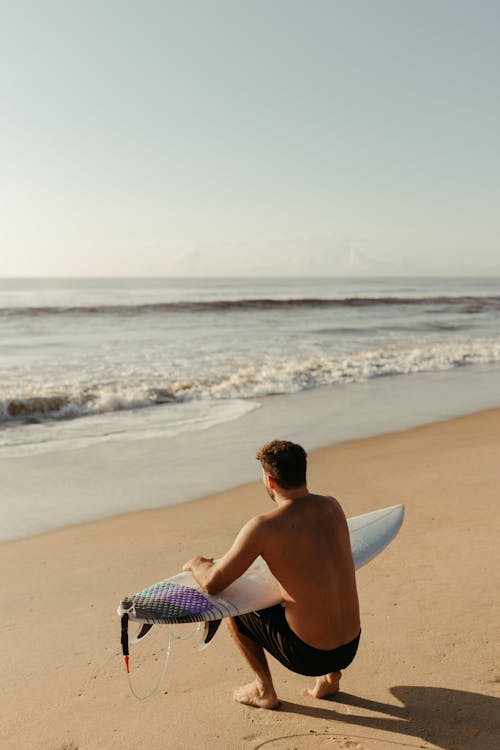 Man Crouching and Holding a Surfboard 
