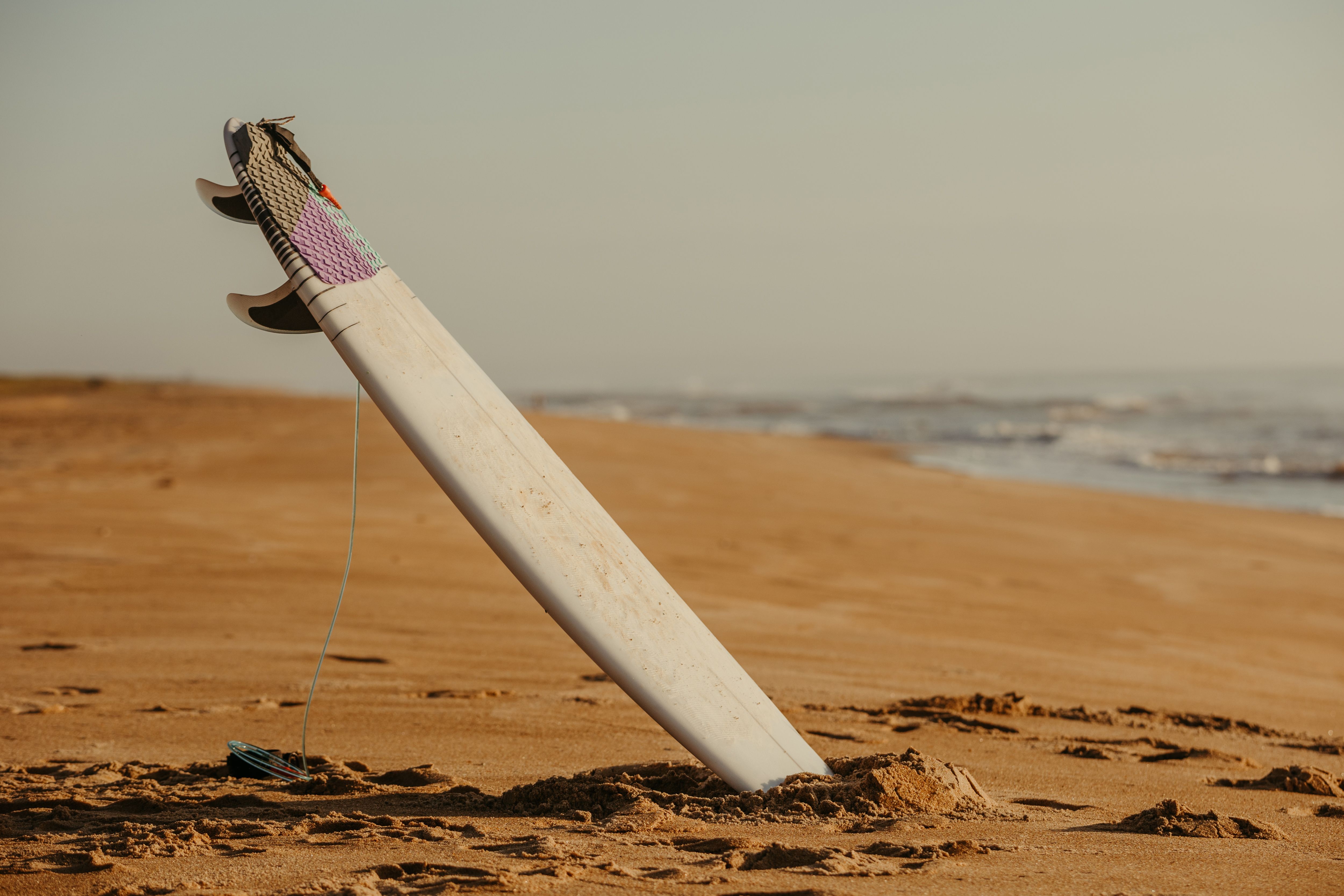 Surfboard standing in sand on a deserted beach, perfect for water sports imagery.