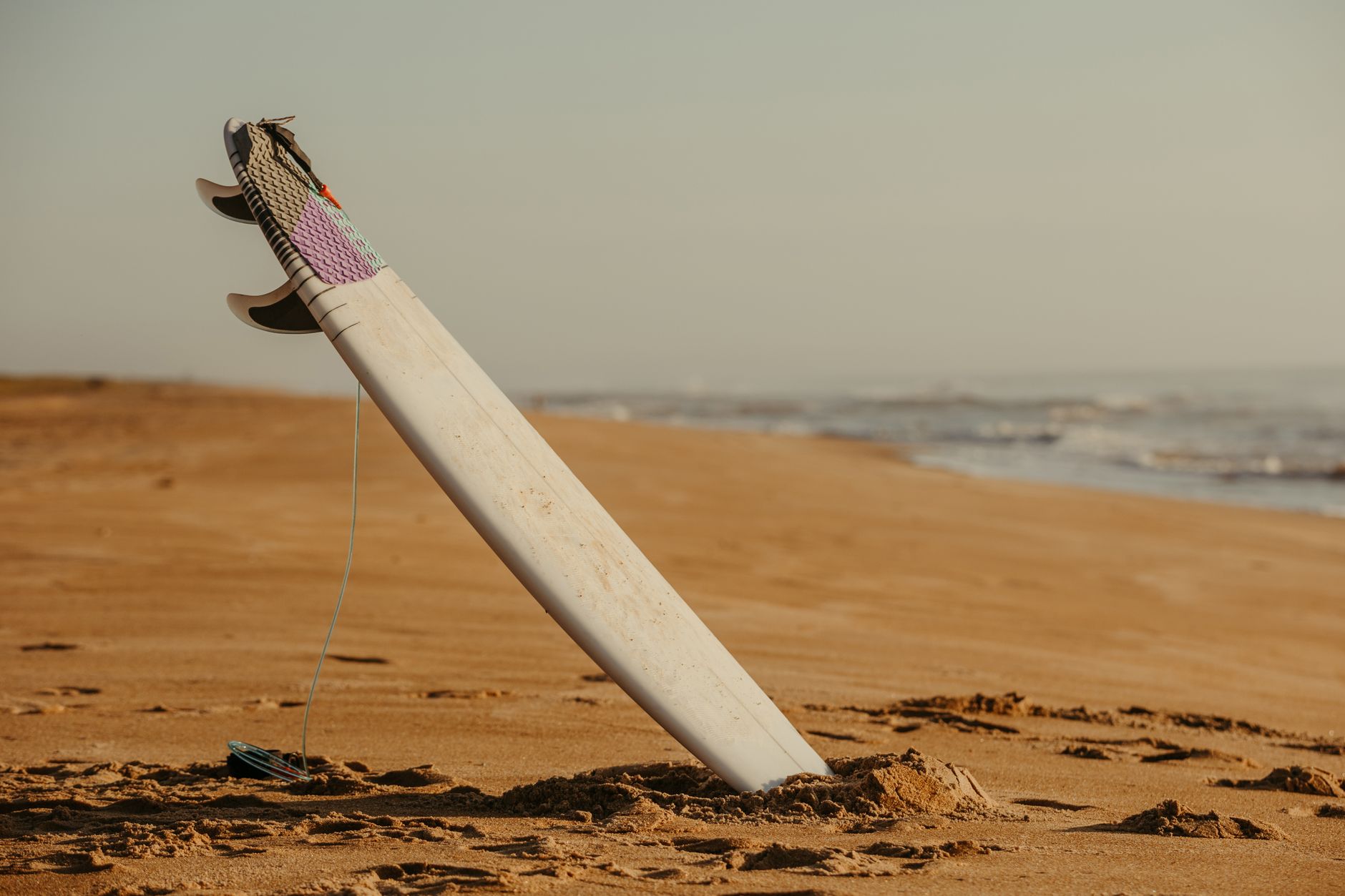 Surfboard standing in sand on a deserted beach, perfect for water sports imagery.
