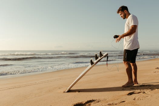 A man stands on the beach preparing his surfboard on a bright summer day.
