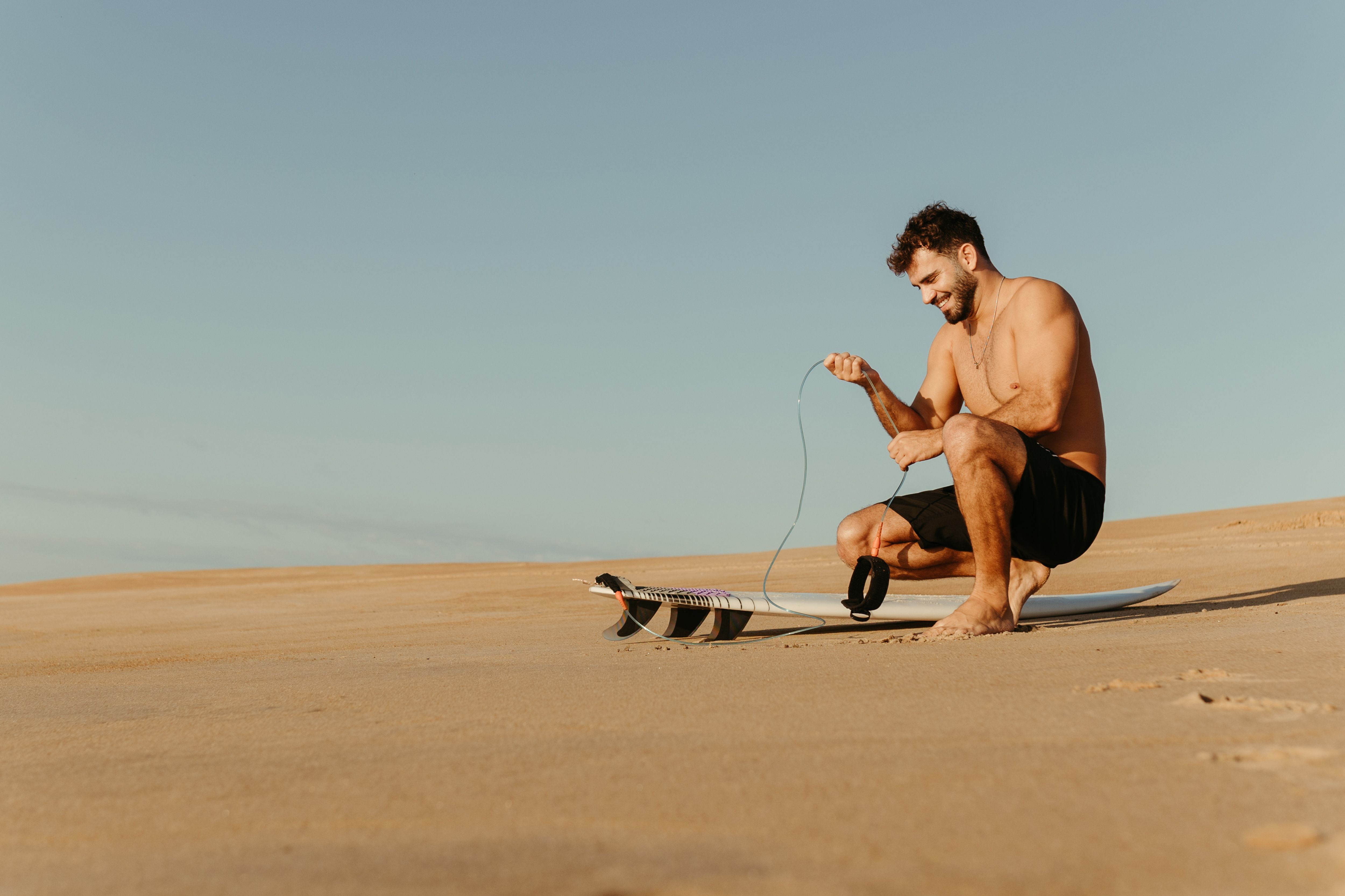 Man Crouching over Surfboard on Beach · Free Stock Photo