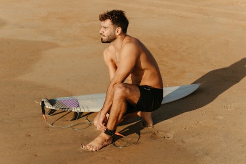 Man Crouching on the Beach with a Surfboard 