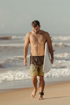 Shirtless man walking on beach carrying surfboard, enjoying summer.
