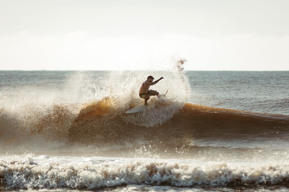 A dynamic action shot of a surfer catching a wave under a clear sky.