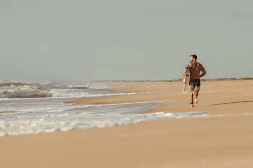 Man Jogging with a Surfboard on the Beach 