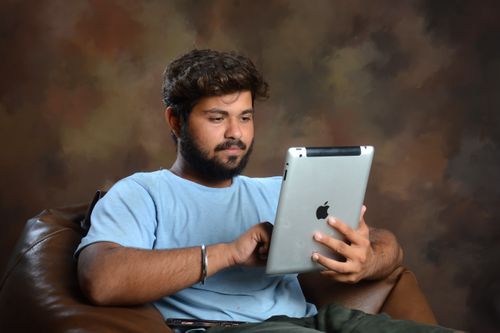 Free Man sitting on an armchair using a tablet, with a warm, artistic background. Stock Photo