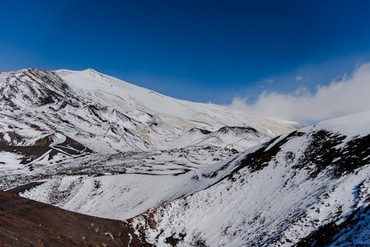 A breathtaking winter landscape capturing the snow-covered slopes of Mount Etna in Sicily under a clear blue sky.