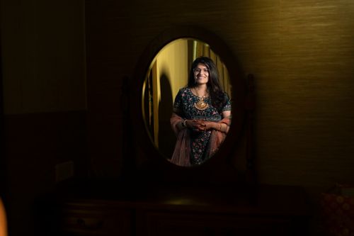 Free A woman smiles at her reflection in a mirror, wearing traditional attire and jewelry. Stock Photo