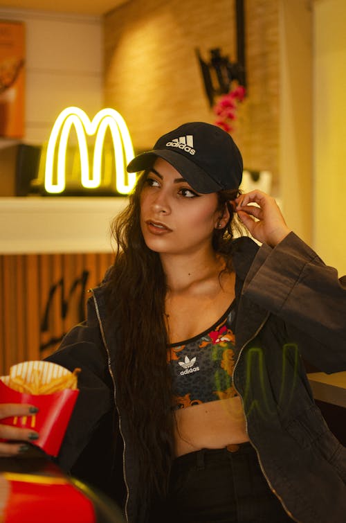 Young Woman in a Baseball Cap Sitting and Eating in McDonalds Restaurant 