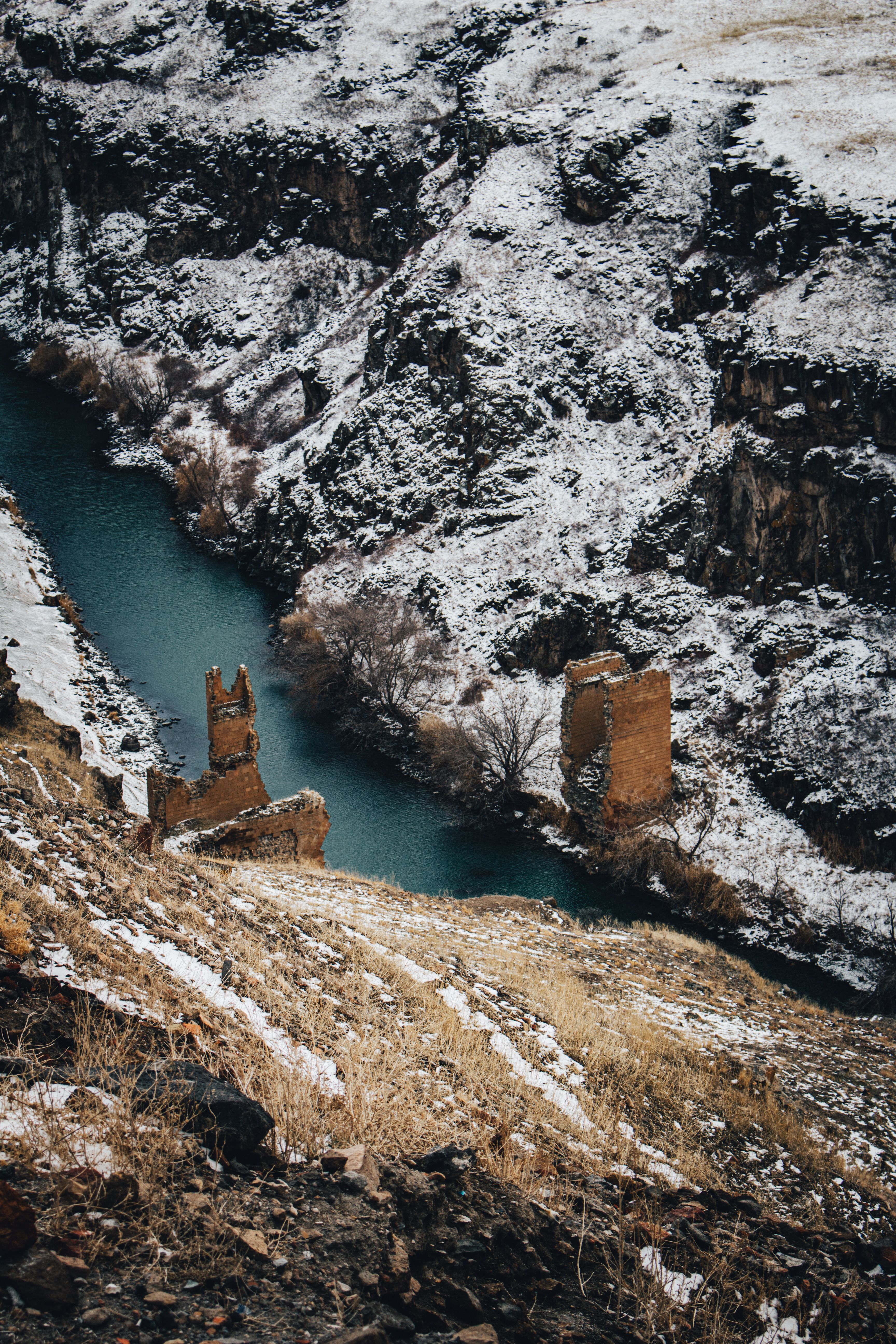 Snow covers medieval ruins and a winding river in a rugged canyon landscape, evoking a sense of history and adventure.