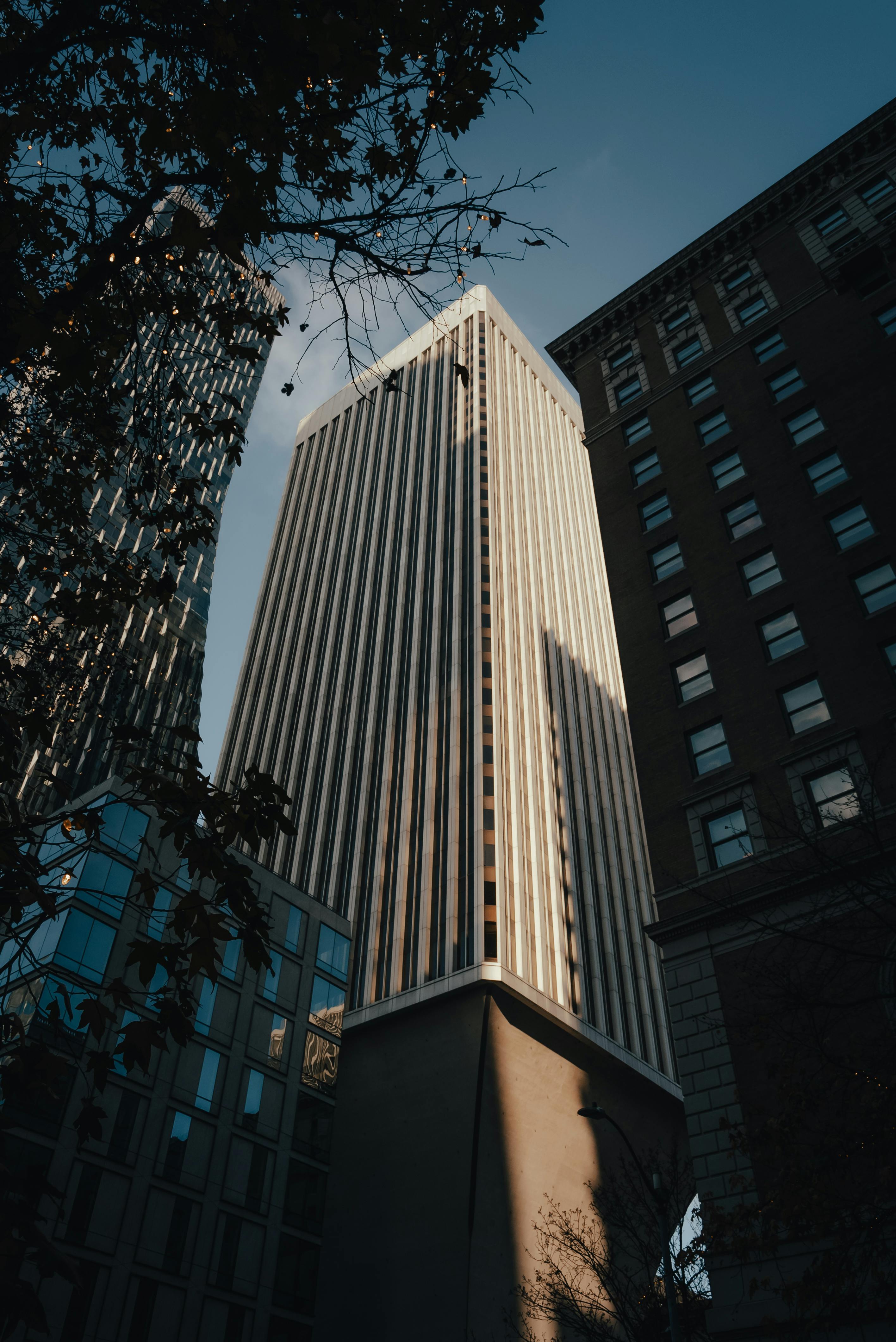 A modern skyscraper in an urban setting bathed in evening light with a dramatic city skyline.