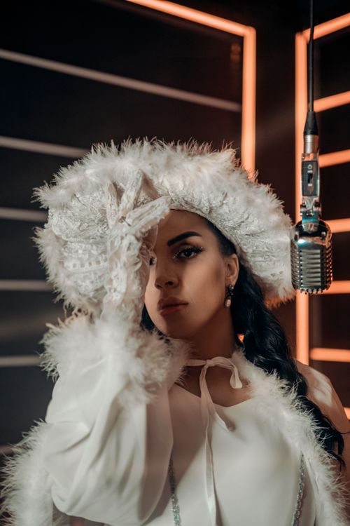 Free Stylish female singer in a luxurious white outfit with a vintage microphone, exuding elegance. Stock Photo