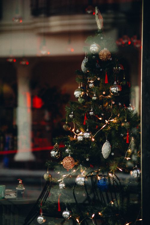 Free A beautifully decorated Christmas tree seen through a café window, creating a festive and warm holiday atmosphere. Stock Photo