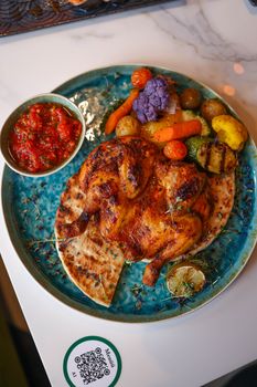 Delicious grilled chicken served with colorful vegetables and flatbread on a blue plate.