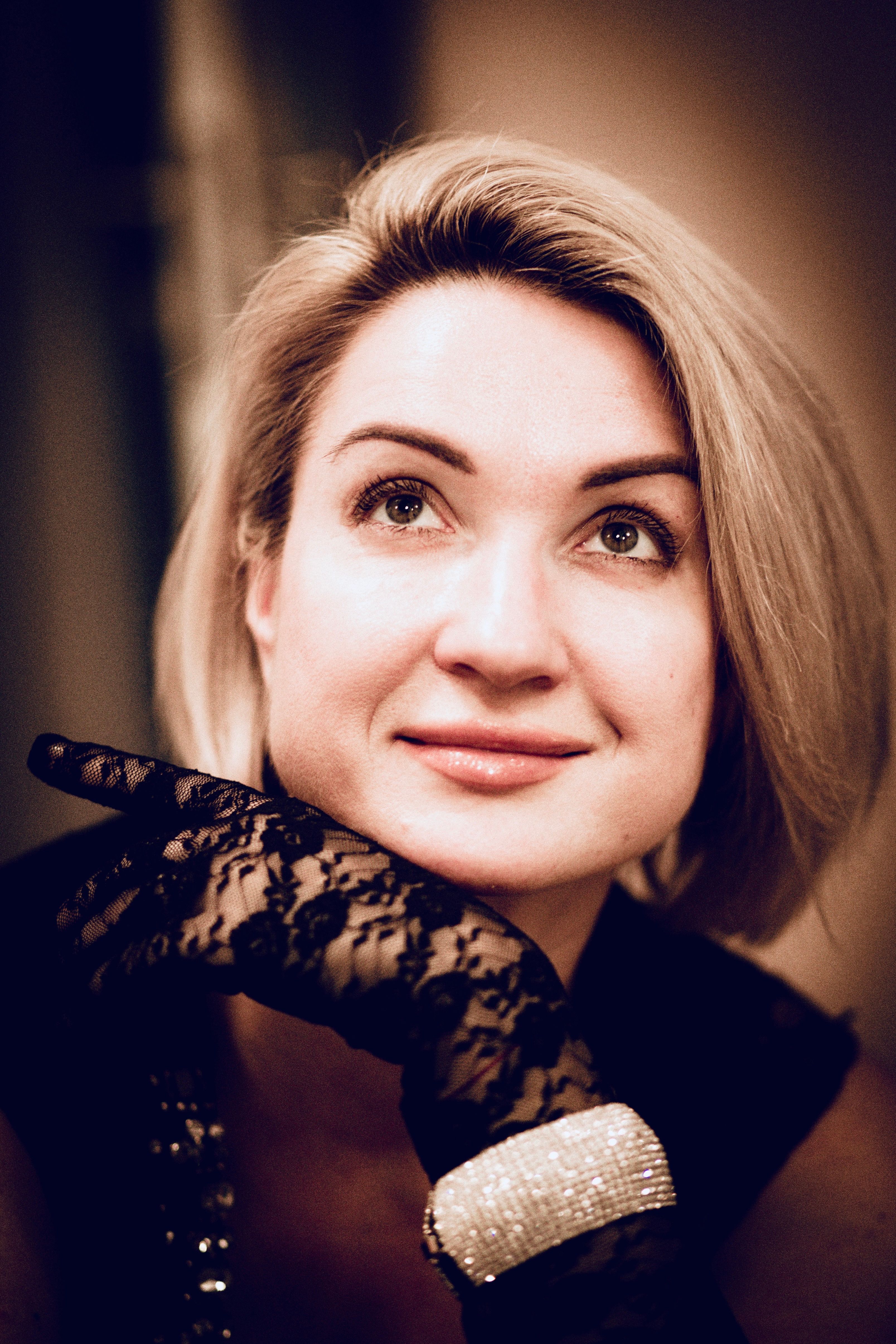 Close-up of a blonde woman with a lace glove looking upward. Captures elegance and style.