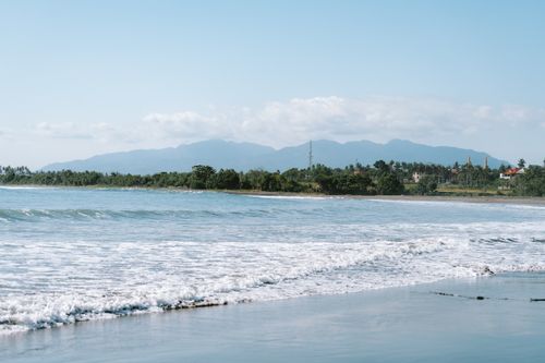 Free Calm beach scene with gentle waves and mountains in Pulukan, Bali, Indonesia. Stock Photo