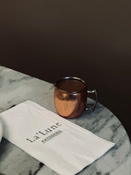 Copper mug on marble table with La'Lune patisserie napkin, elegant cafe ambiance.