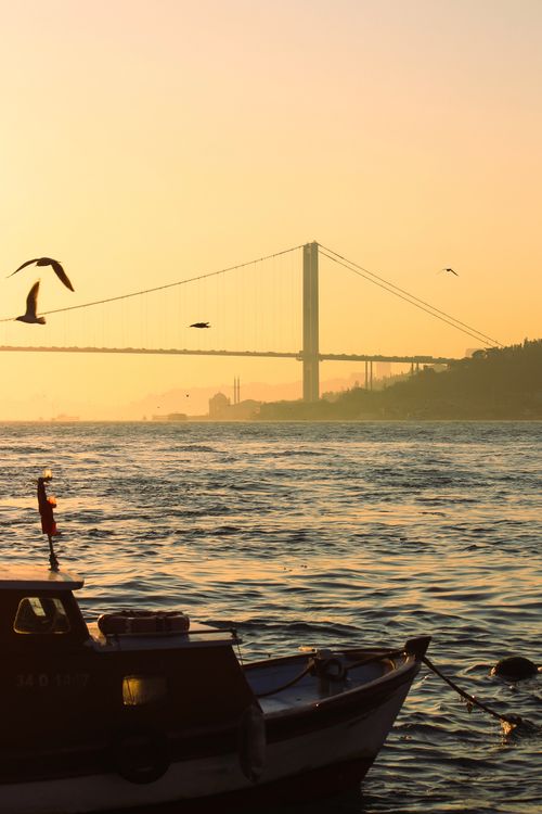 Free Scenic view of a boat and suspension bridge silhouetted against the warm dawn sky. Stock Photo