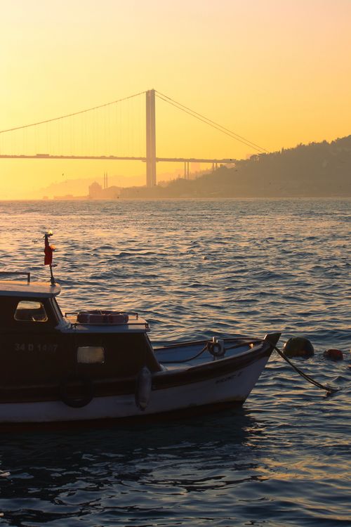 Free A serene view of the Bosphorus Strait at sunset with a boat and bridge in silhouette. Stock Photo