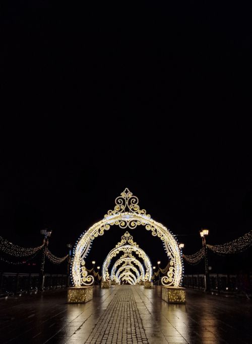 Free A beautifully decorated archway illuminated with golden lights, creating a stunning visual tunnel effect at night. Stock Photo