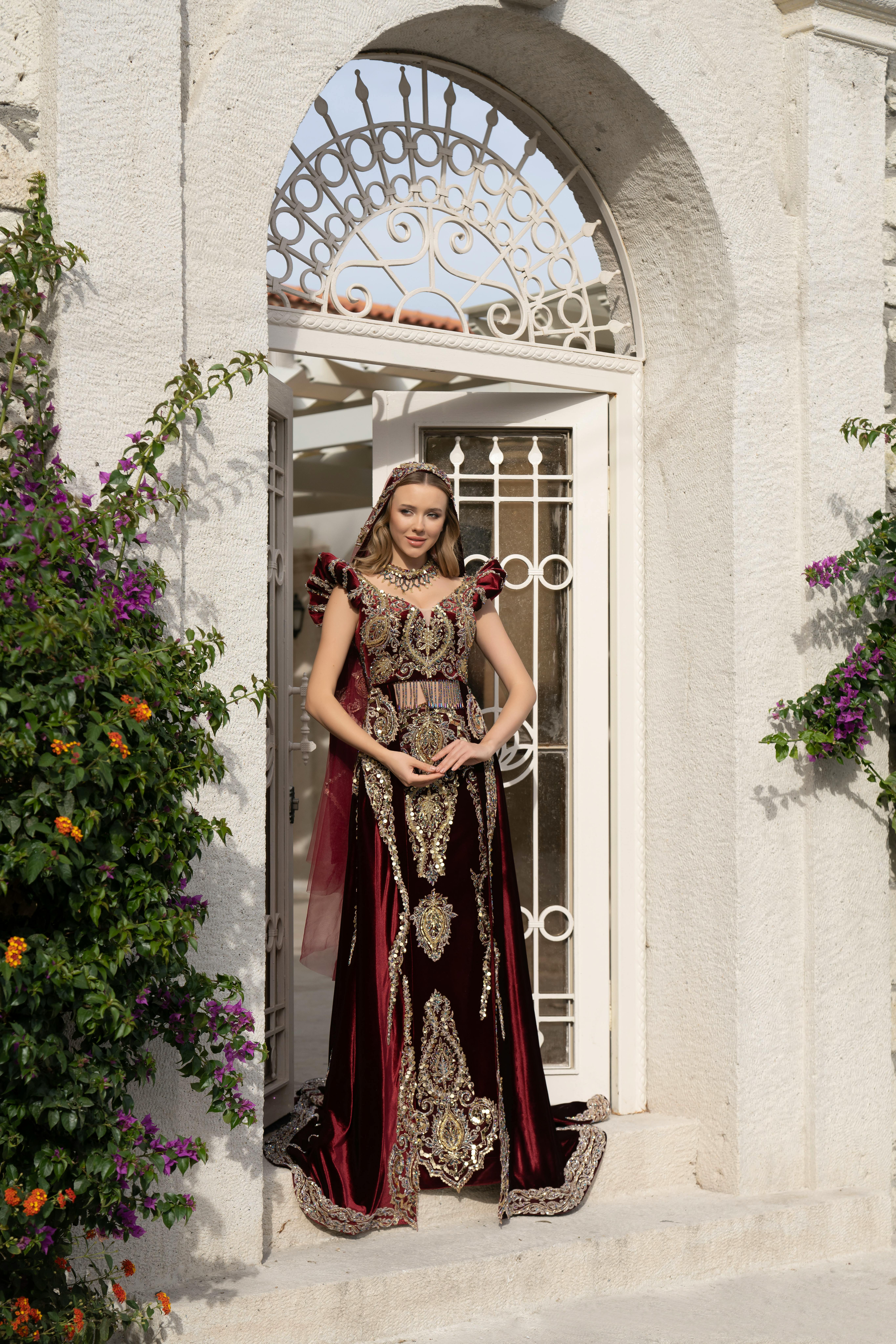 Woman in an ornate traditional bridal dress poses elegantly in front of a vintage İzmir doorway.