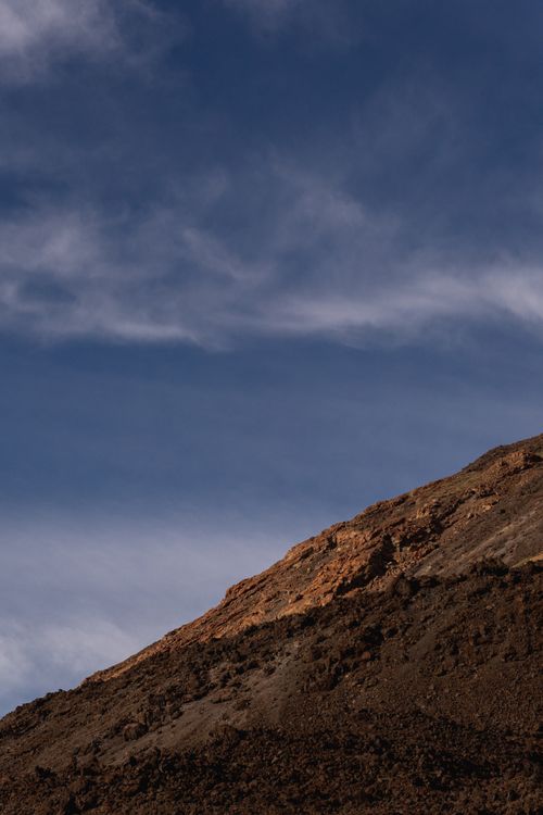 Free A striking view of a rocky desert hillside beneath a blue sky with wispy clouds. Stock Photo