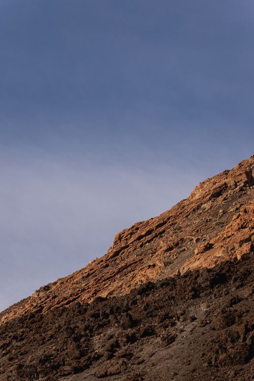 Free Majestic rocky mountain slope with clear blue sky, perfect for a serene landscape wallpaper. Stock Photo