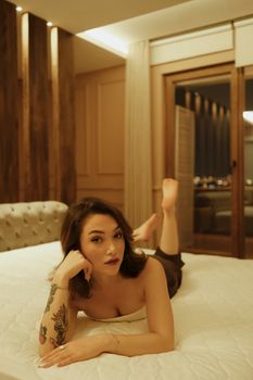 Young woman with tattoos lying on a luxury hotel bed, creating a serene and stylish atmosphere.