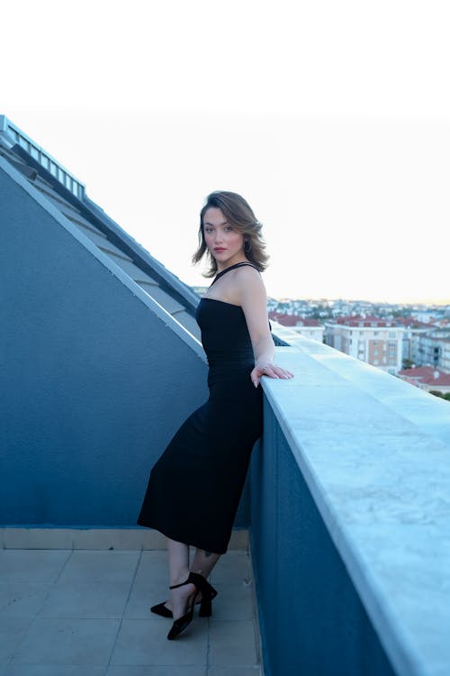 Young Woman in a Black Dress Standing on the Balcony 