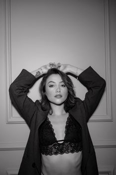 Black and white portrait of a young woman posing confidently in lace lingerie and a jacket.