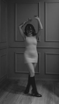 Monochrome image of a young woman joyfully dancing in a stylish indoor setting.