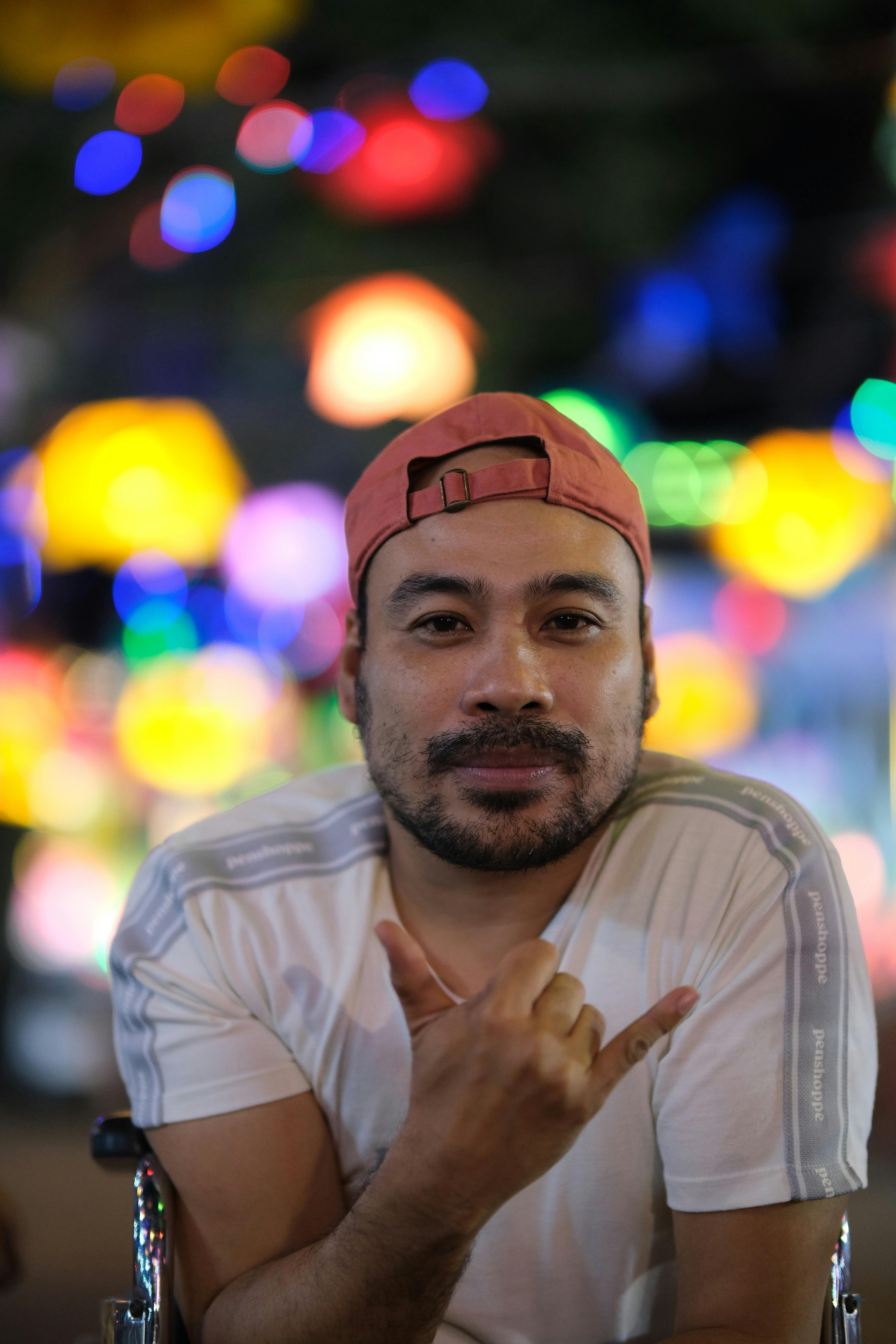 A man in a casual cap poses with colorful bokeh lights at night.
